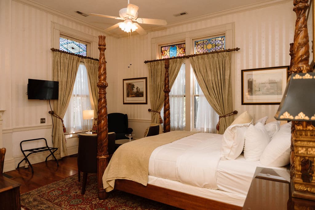 Elegant bedroom featuring a large wooden four-poster bed, stained glass transom windows, and vertical striped wallpaper.