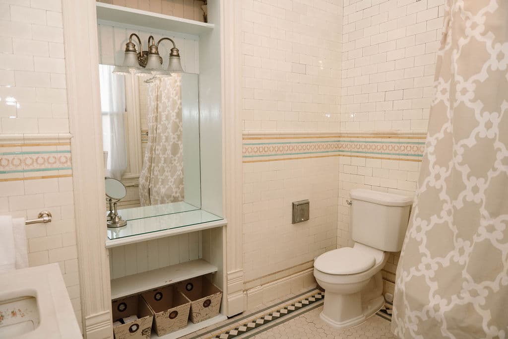 Classic bathroom design featuring subway tiles with a colorful accent border, a built-in vanity shelf with open storage, and traditional mosaic floor tiling.