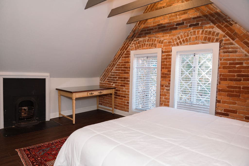 Cozy loft bedroom with exposed brick, ceiling beams, and vintage leaded glass windows.