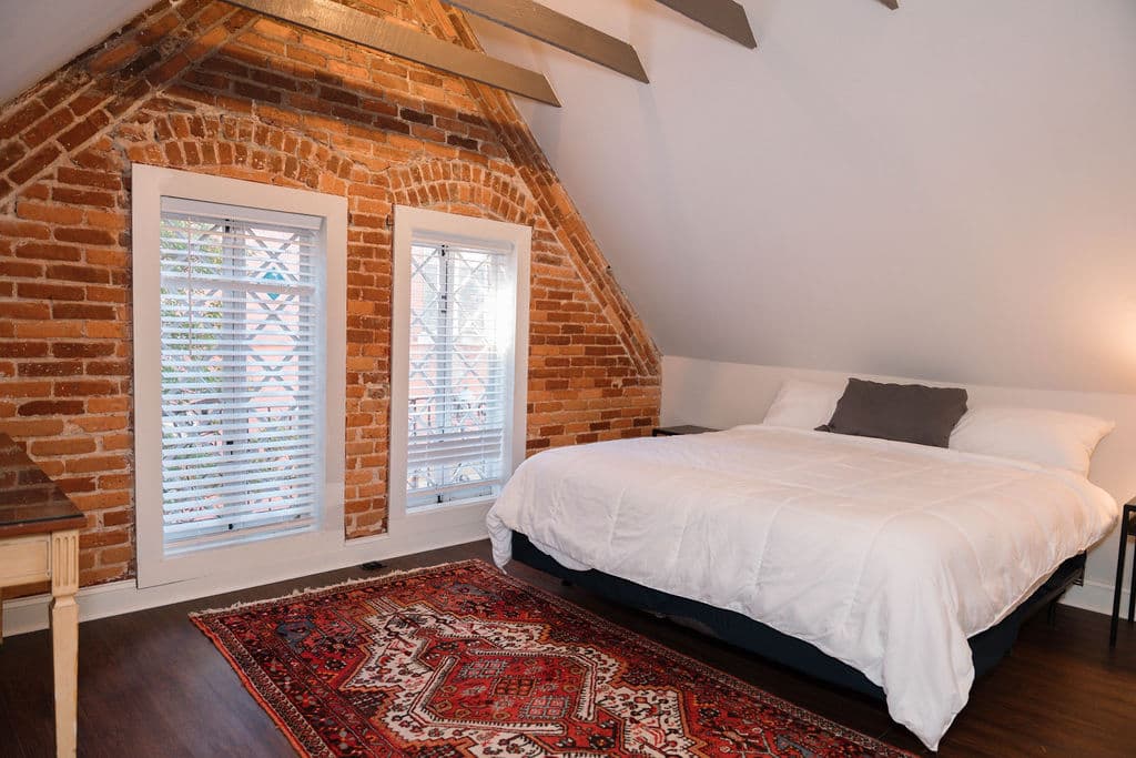 Cozy loft bedroom with exposed brick, ceiling beams, and vintage leaded glass windows.