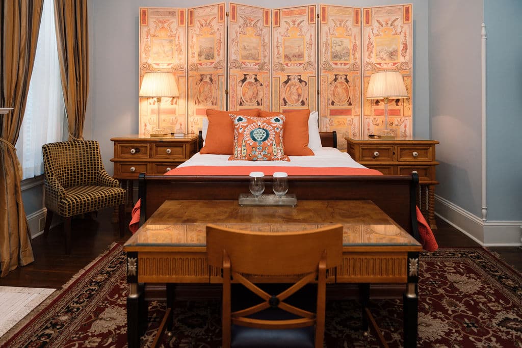 Straight-on view of a bedroom suite featuring a wooden desk in the foreground, a sleigh bed with orange accents, and a large decorative screen behind the headboard.