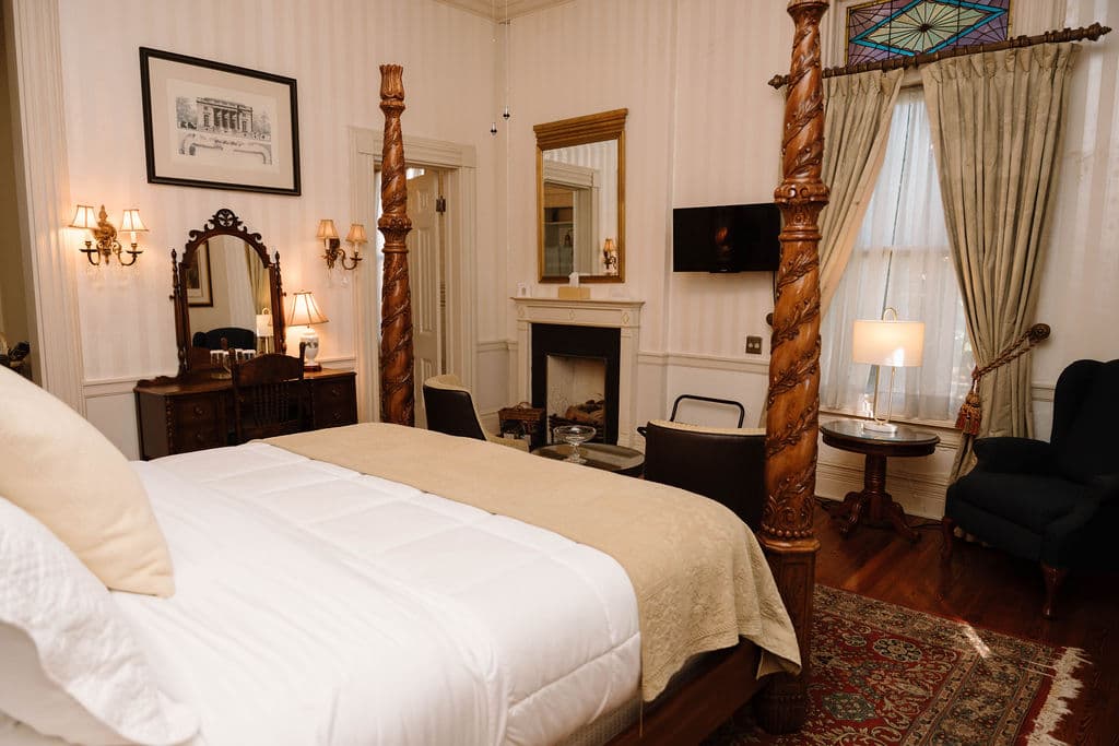 Traditional bedroom with a four-poster bed facing a fireplace and antique vanity.