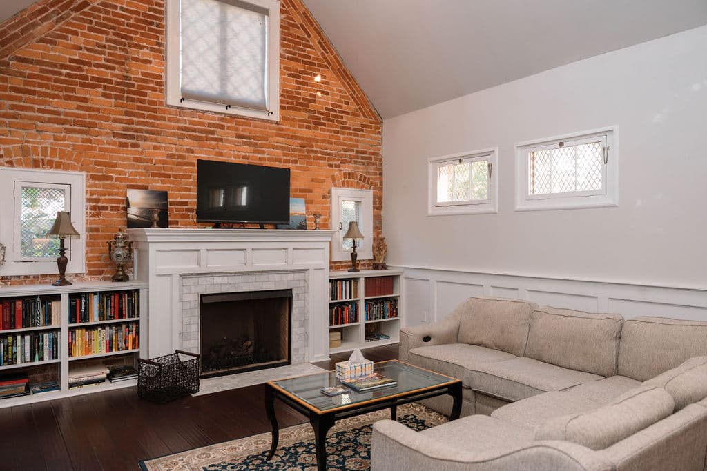 Vaulted living space featuring an exposed brick focal wall, custom millwork bookshelves, a diamond-pane accent window, and hardwood flooring.