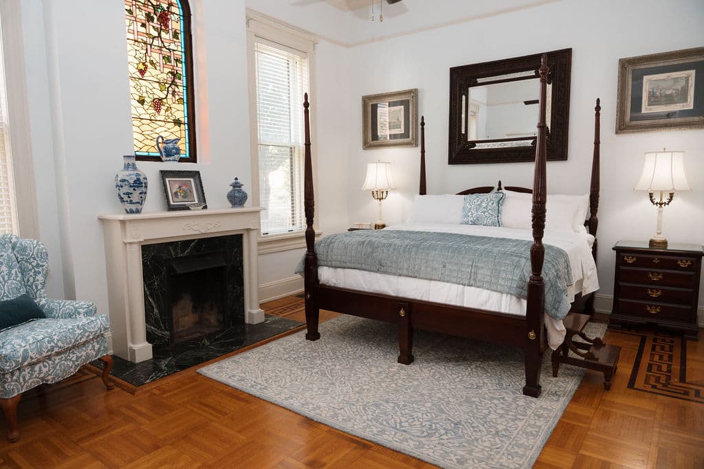 Elegant bedroom with a four-poster bed, fireplace, parquet floors, and stained glass window.