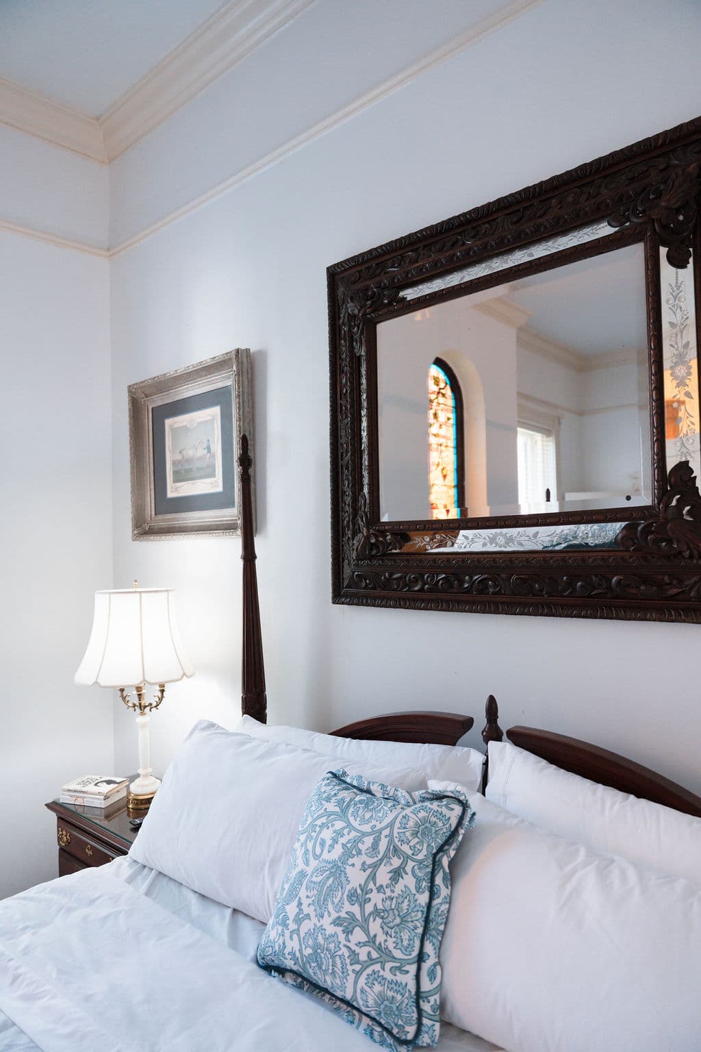 Bedroom detail showing a four-poster bed, blue accent pillow, and large wall mirror reflecting stained glass.