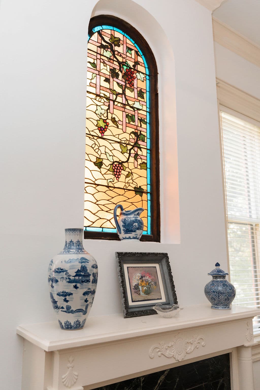 Arched stained glass window detail above a decorated fireplace mantel.