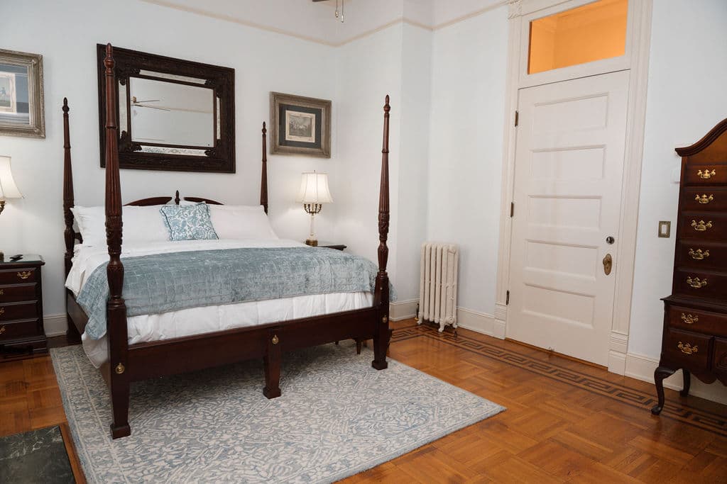 Historic bedroom with parquet floors, four-poster bed, and tall antique dresser.