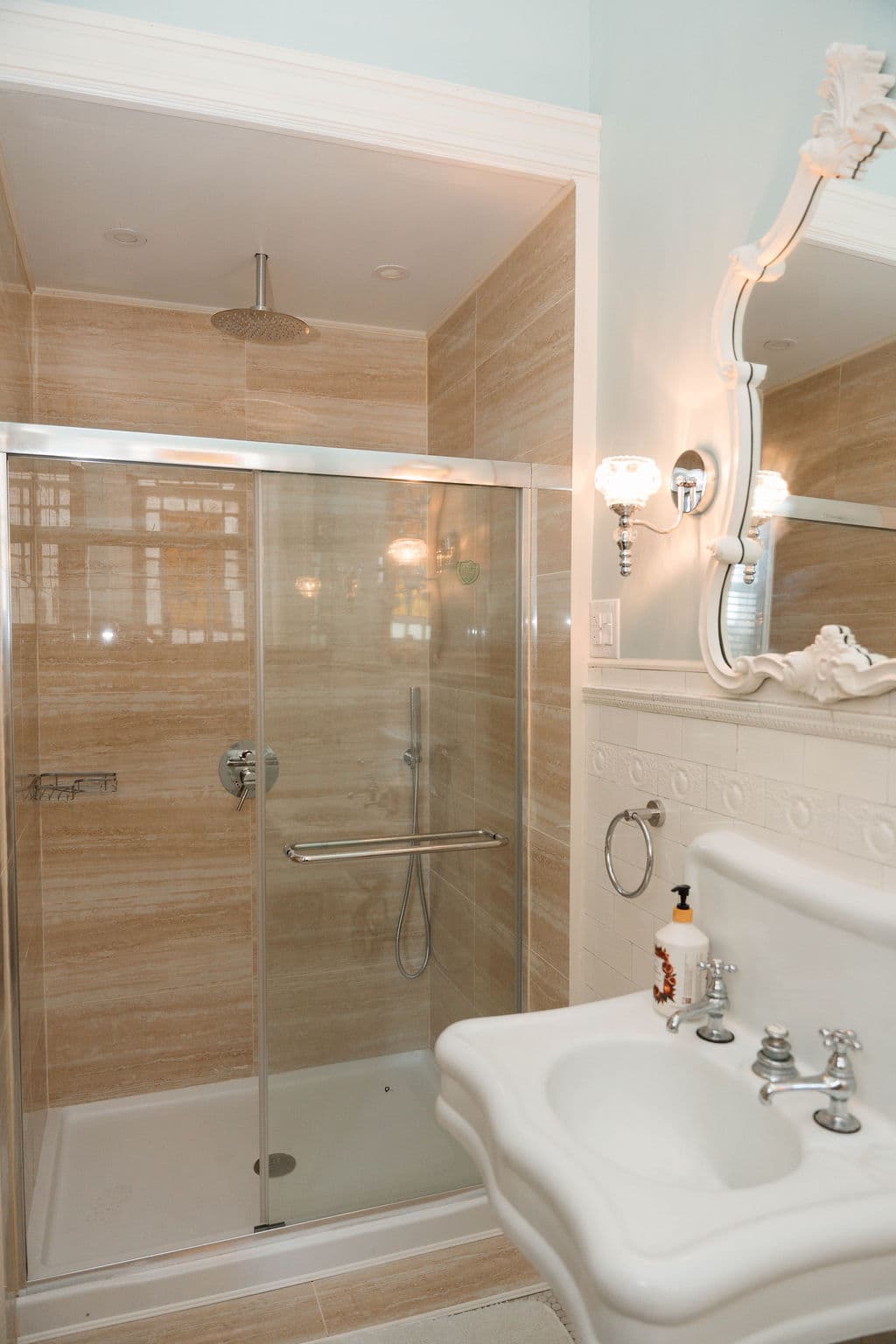 Bright bathroom featuring neutral beige tiling, a glass-enclosed shower with a rainfall head, and vintage-inspired vanity details.