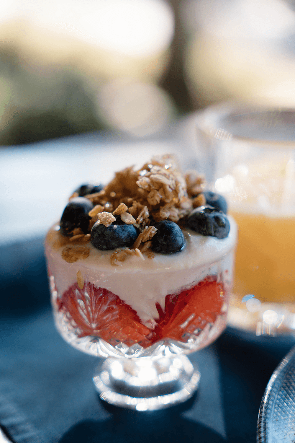 A glass dessert featuring layers of yogurt, strawberries, blueberries, and granola.