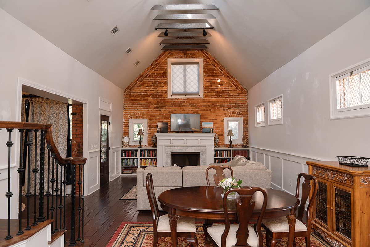 A cozy living room with a high ceiling, exposed brick wall, and a dining area featuring a round table.
